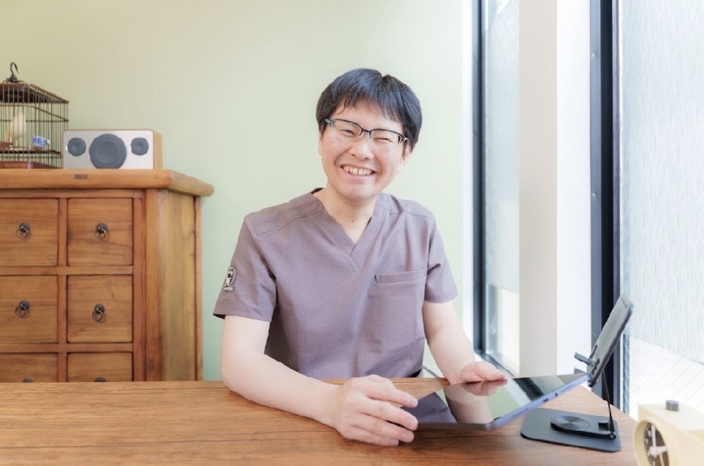 院内の診察室で、デスクに向かい笑顔の施術者。