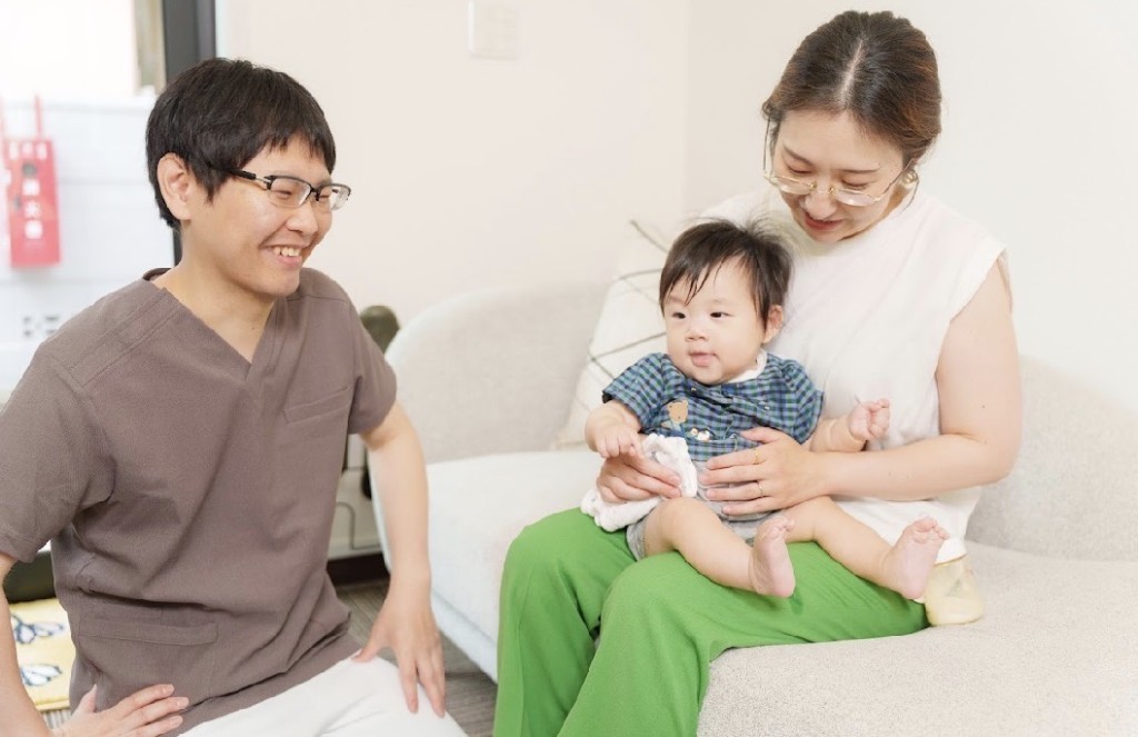 マタニティ鍼灸の施術イメージ。笑顔で話す施術者と、赤ちゃんを抱いてリラックスした様子の母親。