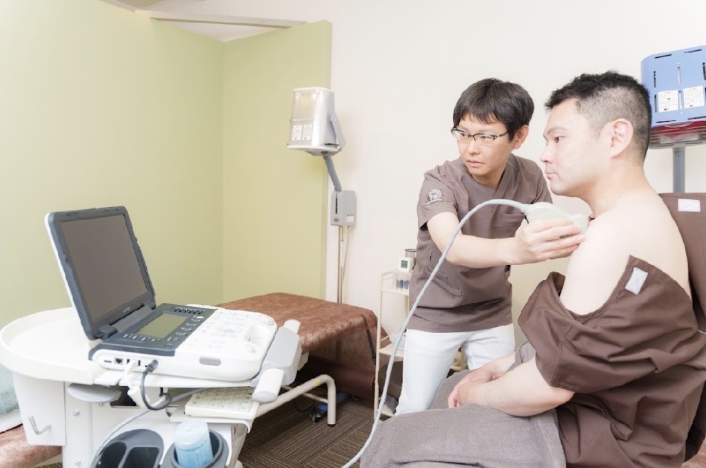 一般鍼灸の施術イメージ。エコー（超音波診断装置）を使用して患者の肩の状態を確認する施術者。